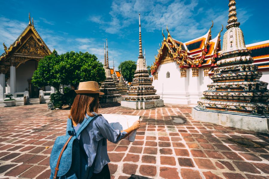 Thailand Bangkok Wat Pho Young woman traveler with backpack and hat looking the map